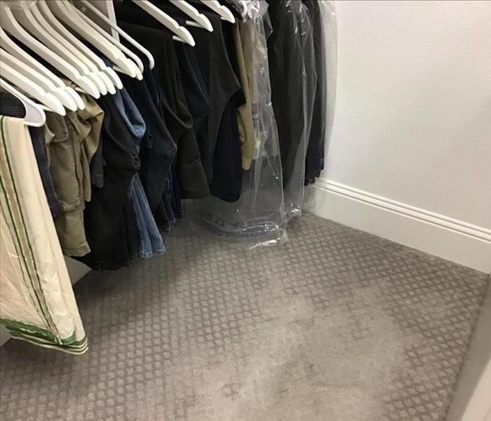 Closet with water damage on the carpet with clothes still hanging up